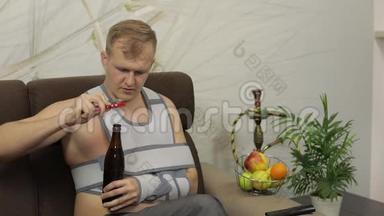 一个手臂骨折的痛苦男人，戴着臂架坐在沙发上喝啤酒