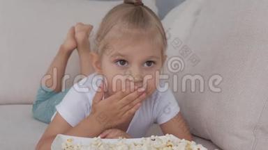 一个小女孩在软榻上吃着爆米花，看着电视<strong>屏</strong>幕。