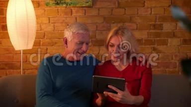 一对年<strong>长</strong>夫妇在平板电脑上浏览<strong>网页</strong>的特写镜头，幸福地坐在舒适的室内沙发上