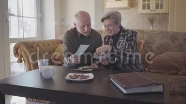 一对成年夫妇坐在沙发上检查他们的旧照片，并分享他们的记忆。 家庭关系。 慢动作。