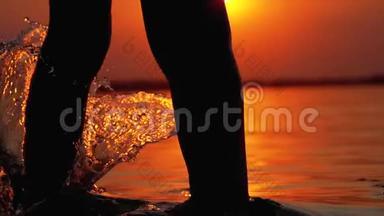 太阳落山时男孩奔跑<strong>入水</strong>的腿剪影，并造成飞溅。 慢动作