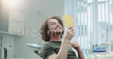 年轻的<strong>牙医</strong>病人坐在蓝色的<strong>牙医</strong>椅上，拿着镜子看着他的牙齿，美白后