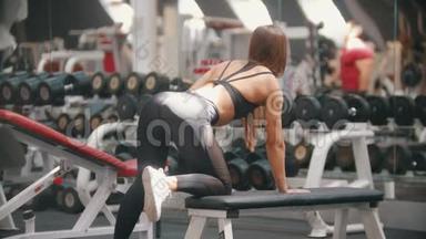 一位运动员女子在健身房<strong>训练</strong>-<strong>训练</strong>她的<strong>手臂</strong>-拉哑铃，同时站在看台上与一个人。