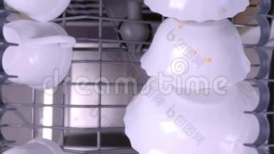 男人`手把一个白色的脏杯和玻璃放在<strong>洗碗机</strong>的上篮里，用厨房用具推着它。