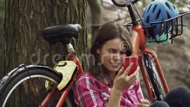 生态自行车运输。 年轻的高加索女学生坐在公园里休息，附近租着橙色自行车，用手机