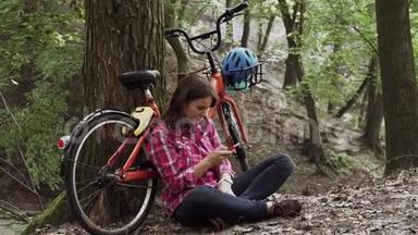 生态自行车运输。 年轻的高加索女学生坐在公园里休息，附近租着橙色自行车，用手机