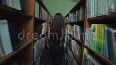 一位留着长长黑发的美丽女孩的后景在图书馆的书架之间，手里拿着书。 慢慢