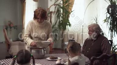 祖母一边为丈夫和两个可爱的孙女们端碗，一边坐着等待