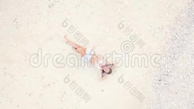 微笑的女人躺在白色的沙滩上，在海滩上鸟瞰。 在度假海滩上放松身心的年轻黑发女人