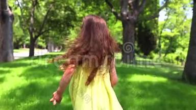 快乐的小女孩穿着黄色连衣裙，光着脚在公园的绿草上奔跑
