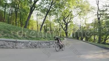 强壮的运动自行车手从马鞍上向上坡冲刺。 骑自行车的人穿着黑色运动服。 慢动作