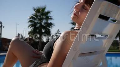 在海滩度假酒店享受夏日，触摸光滑的脱毛腿。 在泳池边晒日光浴的女士