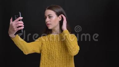 身着黄色毛衣的长发黑发女孩用黑色智能手机快乐地制作自拍照片的肖像