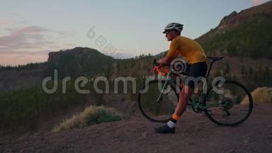 年轻的运动员坐在山顶上的自行车上，戴着黄色的t恤头盔和<strong>运动器材</strong>，看着