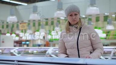 一个穿着冬装的女人在超市里走来走去。 在商店的冰箱里挑选产品