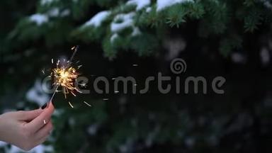 女人手中的孟加拉灯或闪光灯闪烁灯。 背景雪中的圣诞树