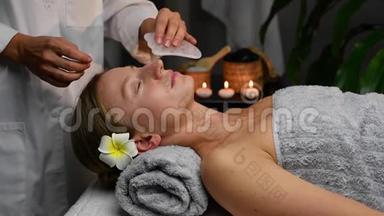 美容师用玉石做专业的面部按摩。 在水疗中心接受面部按摩的妇女