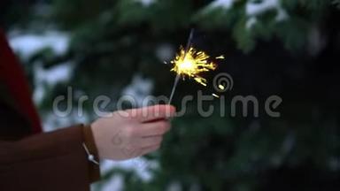 女人<strong>手中</strong>的孟加拉灯或闪光灯闪烁灯。 背景雪中的圣诞树