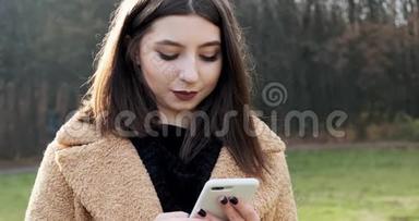 在森林附近的秋天公园，年轻迷人的女人微笑<strong>着看着</strong>智能<strong>手机</strong>的肖像。