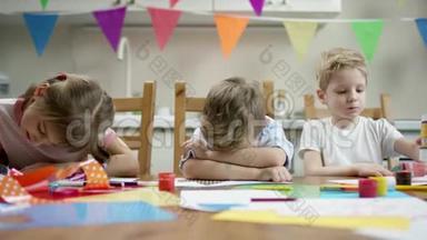 两个男孩和女孩坐在桌边，一个不想画画，除了用铅笔画画
