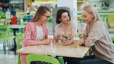 快乐的女士们一起坐在咖啡馆里看着智能<strong>手机屏</strong>幕，然后一起聊天，然后做着击掌和大笑