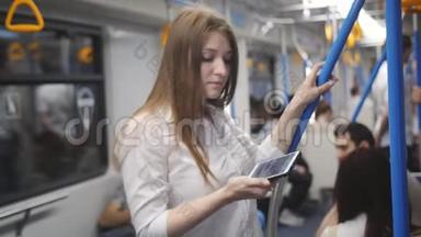 坐地铁的女人用智能手机。 一个女人坐在地铁车上，紧紧抓住扶手，一边走开