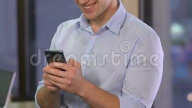 年轻的微笑男子在办公室里滚动智能手机，在约会网站上聊天
