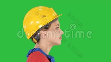 年轻的女工程师带着黄色的安全帽在绿色的屏幕上行走和微笑，铬钥匙。
