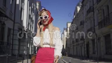 可爱的年轻女子站在街上用手机说话。 有魅力的时髦女孩在老房子里享受阳光