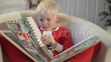 一个英俊的男孩坐在椅子上，用插图读着新年`<strong>童话故事</strong>