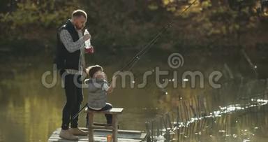 放松时间爸爸和他的爸爸在阳光明媚的日子在湖边钓鱼，教儿子钓鱼，爸爸喝一瓶水。