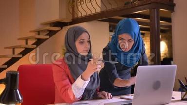 两位身穿头巾的阿拉伯年轻女商人为图中的信息争吵的特写照片