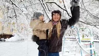 年轻母亲抱着她蹒跚学步的儿子，摇动覆盖着雪的树枝的4k视频。 <strong>家庭娱乐</strong>