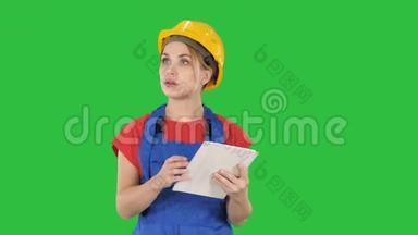 女工程师检查触摸板上的建筑计划，看物体，她周围的建筑在绿色屏幕上，Chroma