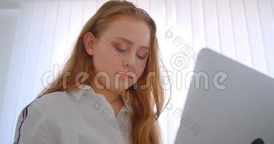 年轻漂亮的白种人女孩的特写照片，她用<strong>笔记本</strong>电脑看着相机，兴高采烈地坐在<strong>上面</strong>微笑