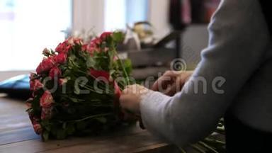 女人`手，在花店里做一束花，一位女士用叶子把蝴蝶结带绑在绿色的茎上。
