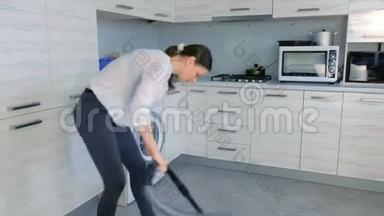 女人用吸尘器打扫厨房地板。 她整理了散落在灰色瓷砖上的玉米片。