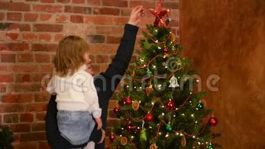 手上抱着可爱女儿的年轻父亲正在装饰圣诞树。新年快乐。父亲节。
