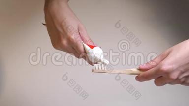 白色刷毛的环保牙刷与新鲜的白色牙膏。 用手捏住木制牙刷上的牙膏