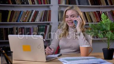 金发白种人的女商人在智能手机上交谈，在<strong>书架背景</strong>下的<strong>办公室</strong>里换座位。