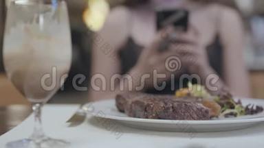 美味的牛排，蔬菜和<strong>叶子</strong>躺在盘子里，在餐厅的女人面前。 `<strong>女士</strong>的手在发短信