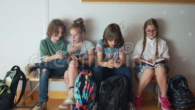 小学生和小玩意。 三个青少年对他们的<strong>手机</strong>充满热情。 尊敬的学生女孩坐<strong>着看</strong>书
