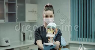 一位年轻的女医生戴着外科口罩和手套，在现代诊所的房间里举着一个巨大的人类头骨和