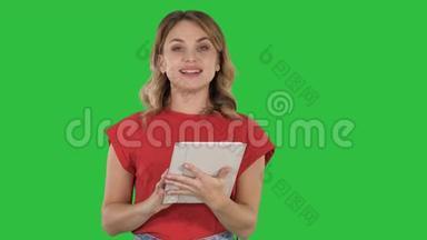 主持人女士穿着红色T恤，拿着平板电脑翻页，在绿色屏幕上与相机交谈，Chroma键。