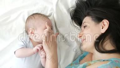 一位美丽的年轻母亲和两个月的新生儿躺在床上互相看着。 妈妈轻轻地