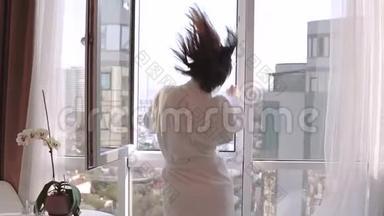 漂亮的黑发女人穿着白色浴袍，享受她的新公寓度假。 快乐的女孩跳舞和跌倒