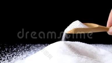 白砂糖在木勺上，在黑色背景下堆积成堆。