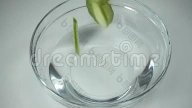 新鲜的黄瓜片掉进玻璃碗里，水站在桌子上，慢动作
