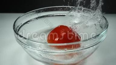 在白色背景下从落下的成熟<strong>番茄</strong>中溅出干净的水，慢动作。 在玻璃碗里放一个<strong>红番茄</strong>