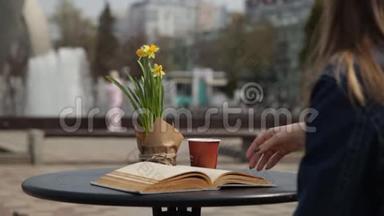 年轻女子喝着咖啡，读着一本书，在一个俯瞰喷泉的咖啡馆的桌子上<strong>翻阅</strong>着书页